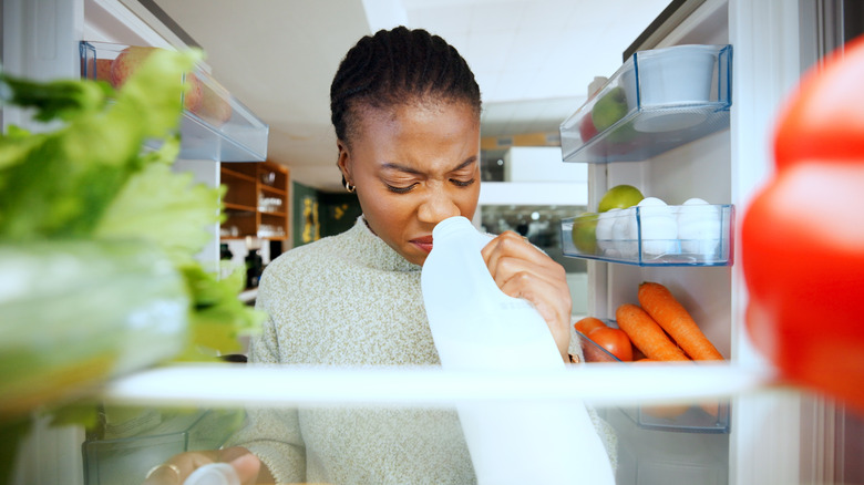A woman smelling a foul odor from a jug of milk