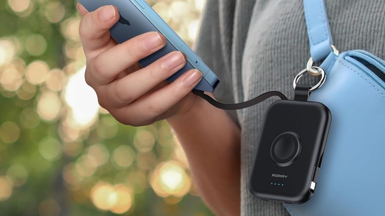 A person charging a phone with a Rorry CharmGo Portable Charger attached to a bag.