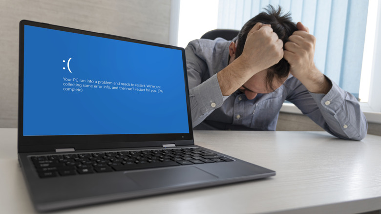 Laptop displaying blue screen of death with anguished man in background