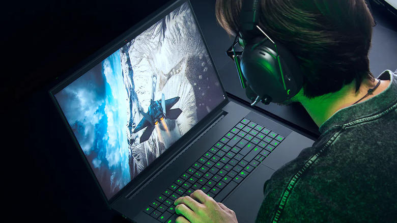 A person gaming on a Razer laptop with green backlit keys and a flight game on screen.