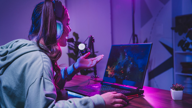 A woman playing DOTA 2 on a gamding laptop under purple lighting