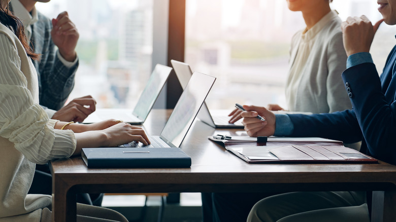 A group of office workers sitting on a table with laptops in front of them