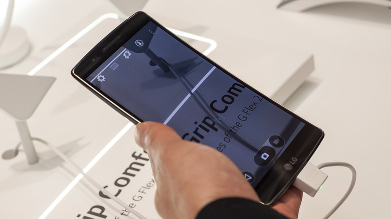Close-up of a hand holding an LG G Flex 2 connected to a display cable.