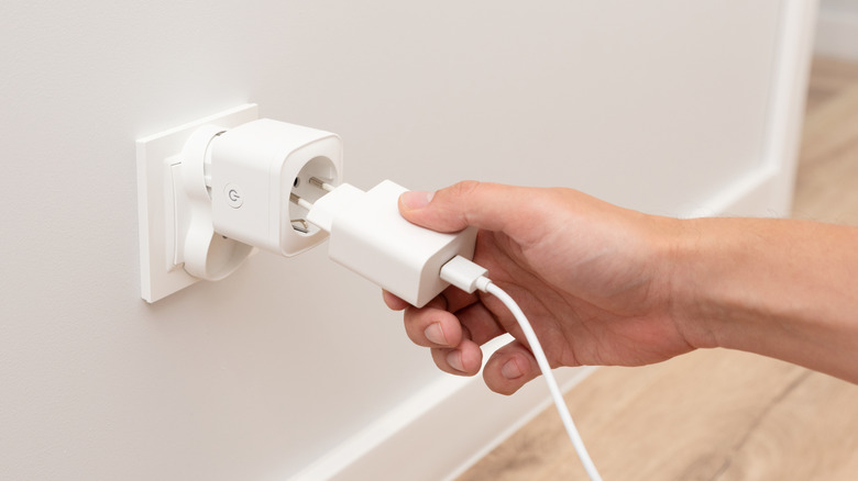 A hand plugging a cord and adapter into a smart socket.