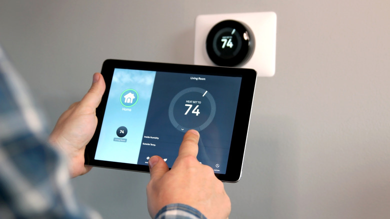 A hand with a tablet adjusting a smart thermostat on the wall.