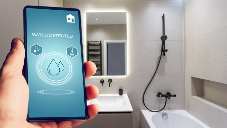 A hand holding a phone with a water detection notice, a bathroom in the background.