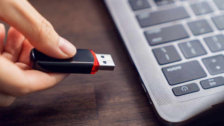 Hand holding usb flash drive with connecting to laptop at wooden table.