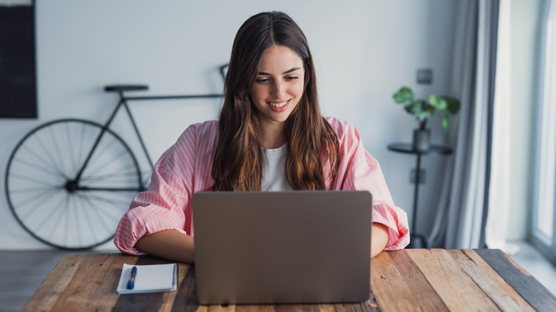 A young woman works on a laptop with a bicycle in the background