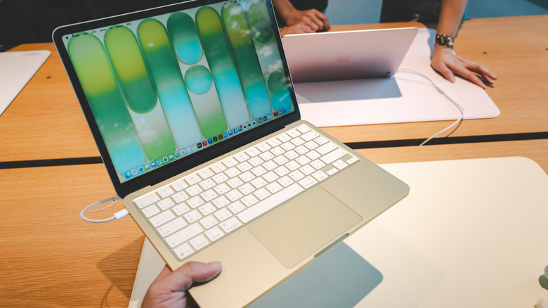 A hand holding a MacBook Neo in an Apple Store