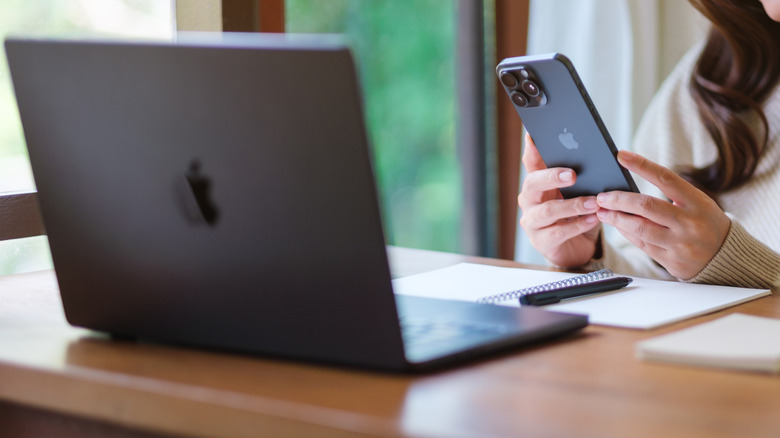 A person using an iPhone and MacBook at a desk