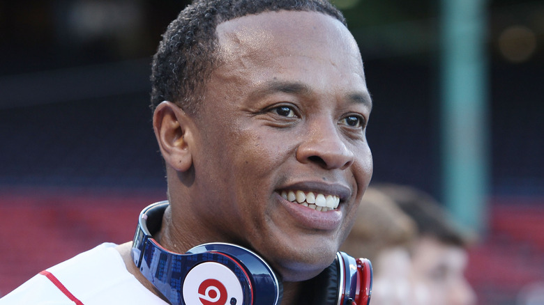 Artist Dr. Dre with a pair of Beats headphones around his neck, the rapper appears to be at a baseball game, though the background is heavily blurred