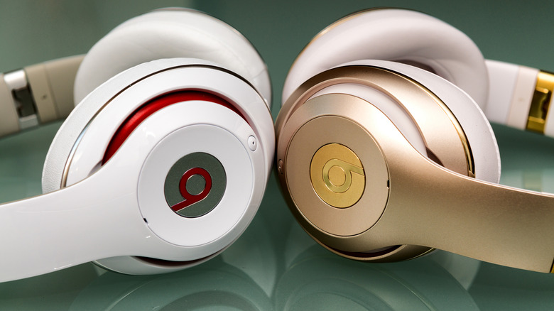 Two pairs of Beats Studio wireless headphones - one pair white with red trim and other other gold with white trim - sitting on a glossy green surface