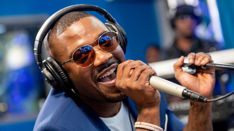Artist Ray J wearing a pair of black over-ear headphones as he wears a blue blazer and sing into a microphone