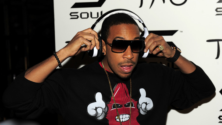Actor and rapper Ludacris wearing a black sweatshirt and standing in front of a promotional sign for Tao Nightclub in Las Vegas and Soul Electronics, Ludacris is adjusting a pair of black and white headphone
