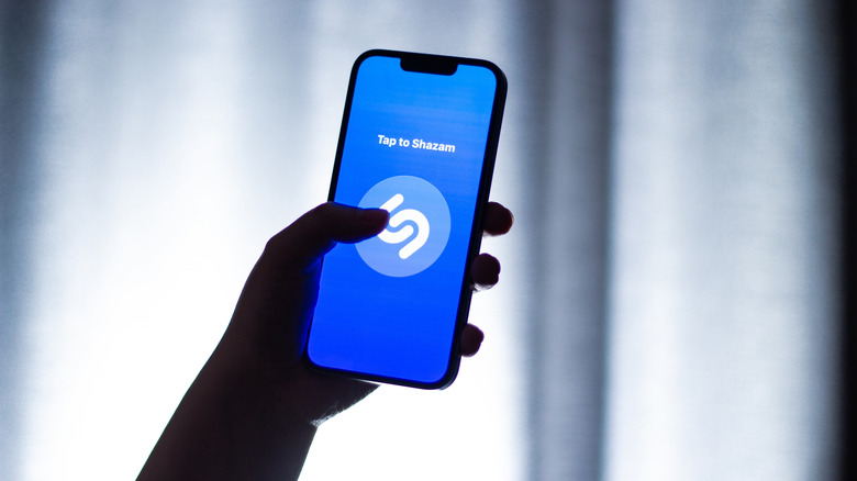Woman holds smartphone showing Shazam logo on screen. Music application