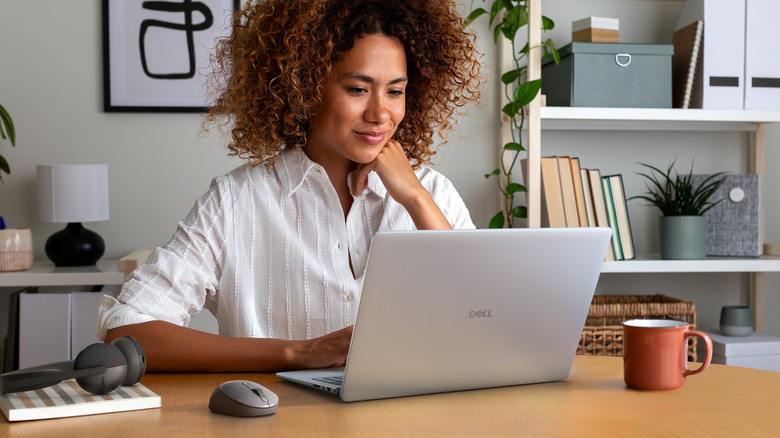 A person using the Dell 16 laptop on theior desk with other gadgets around