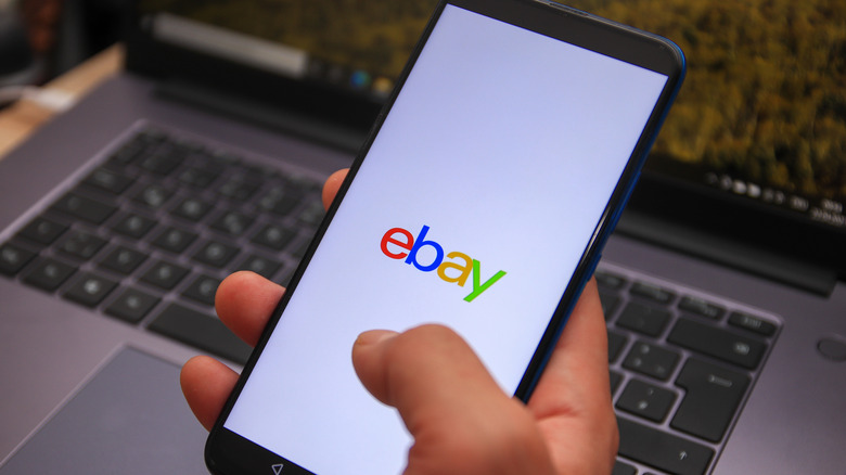A person holding a smartphone with the eBay logo.