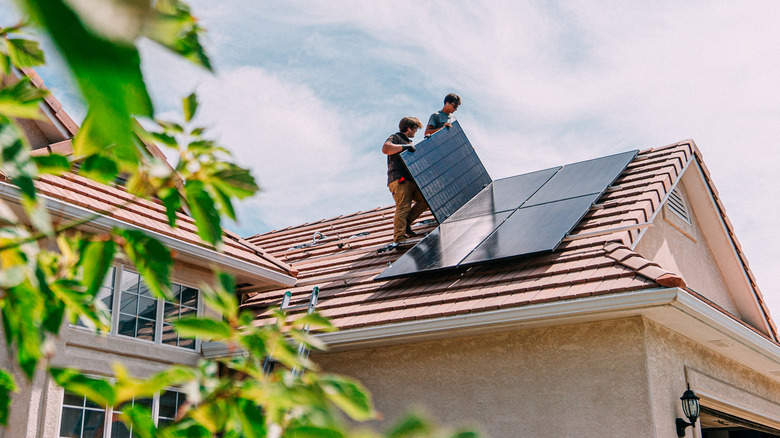 Two solar installers placing a panel on a residential roof.