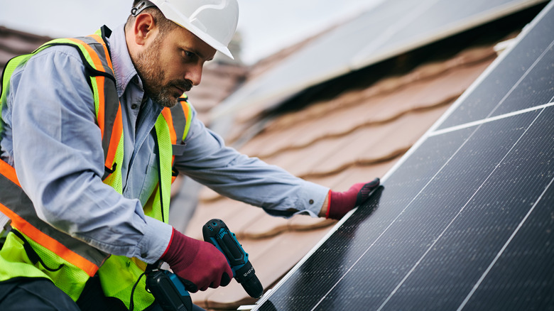 Solar panel installer securing a rooftop panel with a drill.