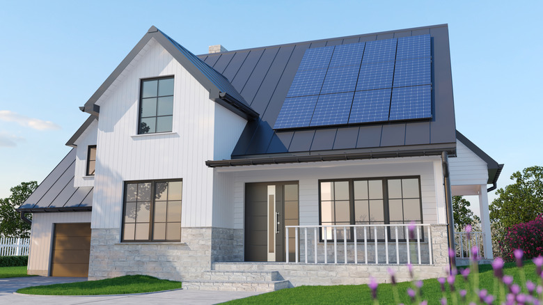 Modern white house with solar panels installed on a dark roof under a clear blue sky.