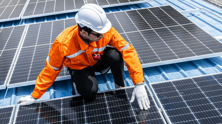 Solar technician inspecting rooftop solar panels while wearing a hard hat and orange safety jacket.