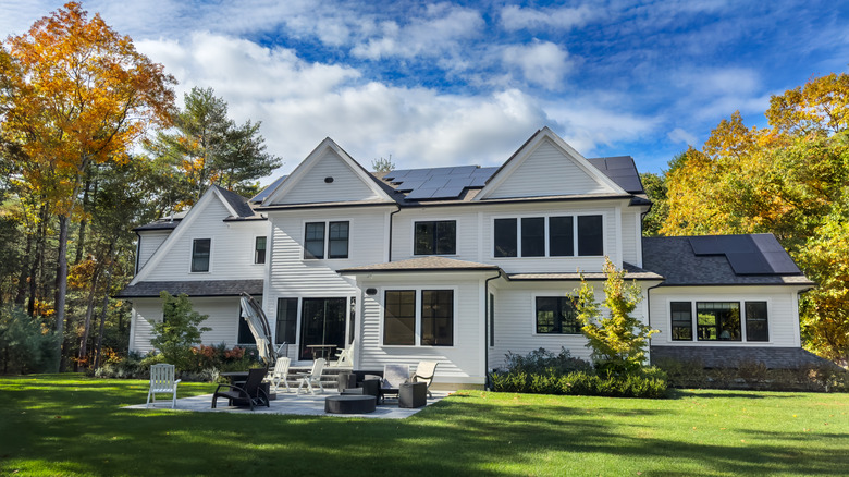 White house with solar panels on the roof and a patio in the backyard.
