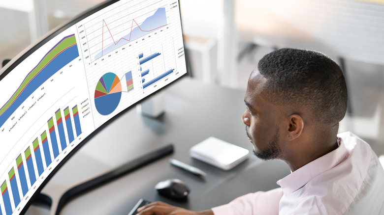 Person analyzing charts and graphs on a curved monitor.