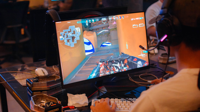 Person playing a shooter game on a PC with keyboard and headset.