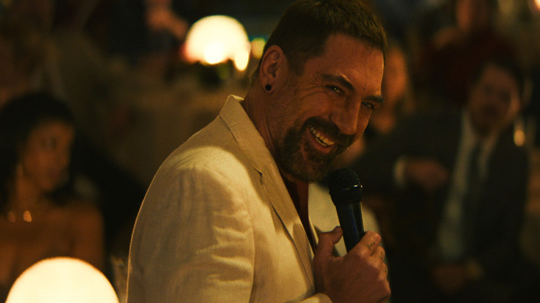 Max Cady (Javier Bardem), clothed in a linen white suit, cackles into a microphone as he gives a speech at an event in Cape Fear