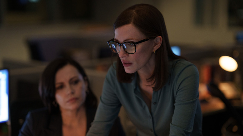 Jodi, wearing glasses and a blue shirt, busies away at an unseen computer while a coworker looks on.