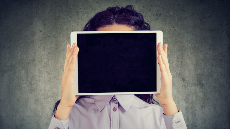 A person hiding their face with a tablet.