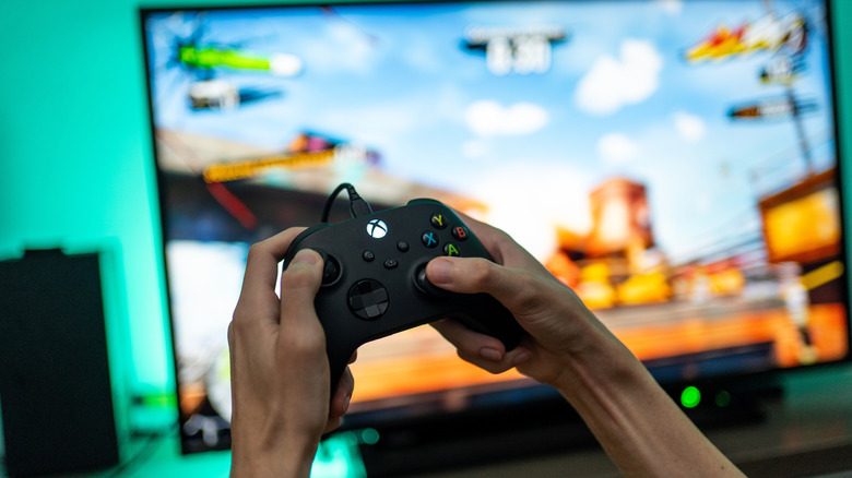Person holding an xbox controller, with video game on blurred monitor in background