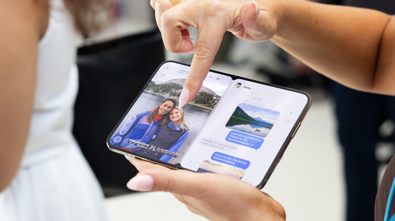 person using iPhone Duo, pointing at photo with messages open on other side of display