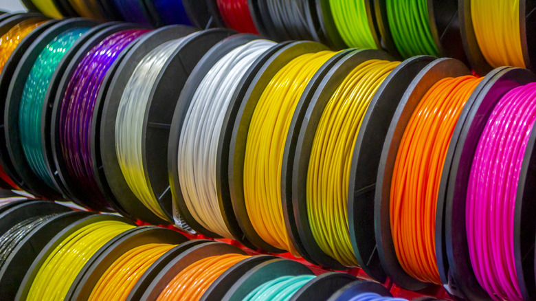 Colorful 3D printer filament spools arranged on shelves.