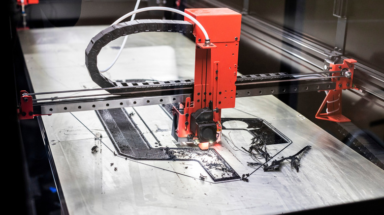 3D printer laying black filament on a large print bed.