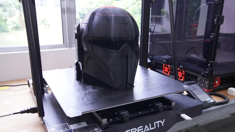 Creality 3D printer creating a black sci-fi helmet on its build plate.