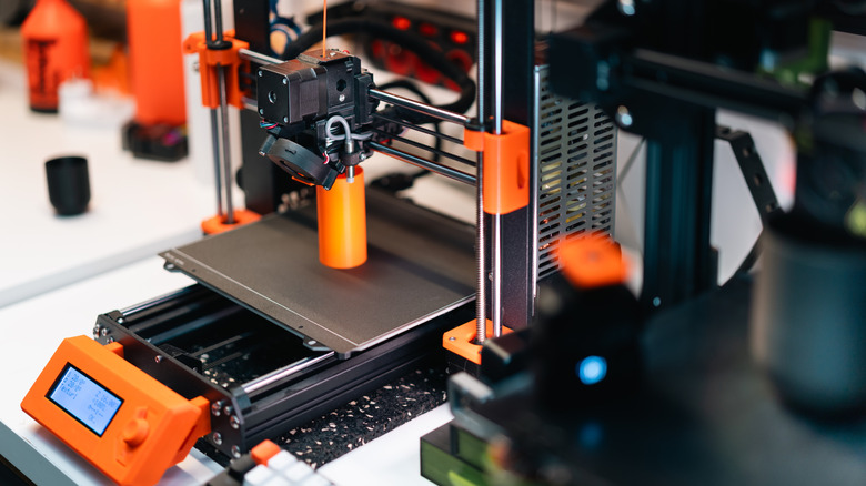 3D printer creating an orange object on its print bed.