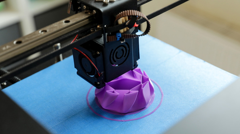 3D printer creating a purple geometric model on a blue print bed.
