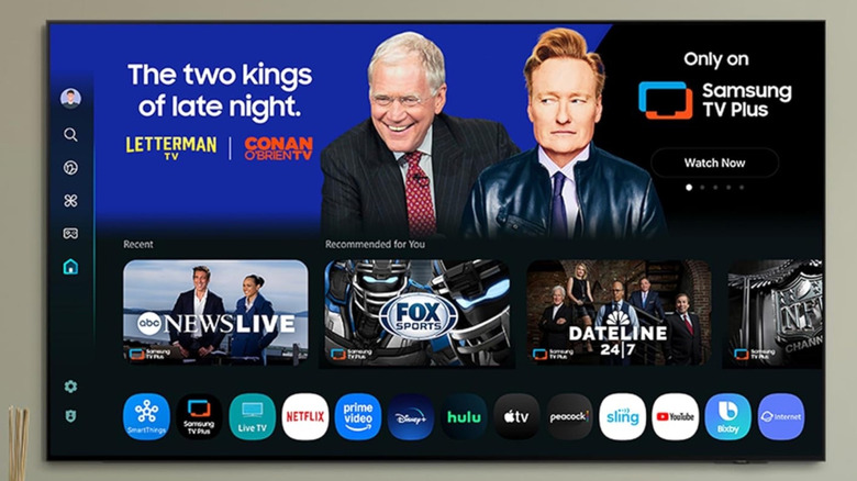 The Samsung QN90F wall-mounted in a living room showing a Samsung TV Plus promo