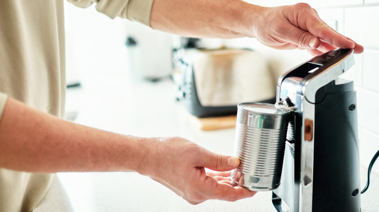 A person using a countertop electric can opener.