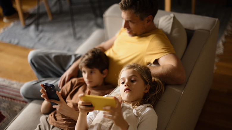 Dad with his children who are on modern gadgets.