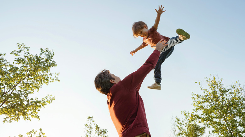 Dad playing with son outdoors throwing him in the air.