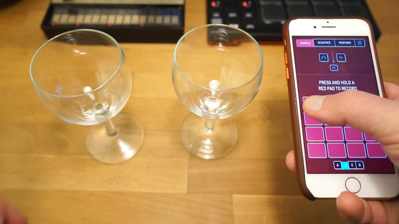 A person using Koala Sampler on their phone that's placed near two wine glasses