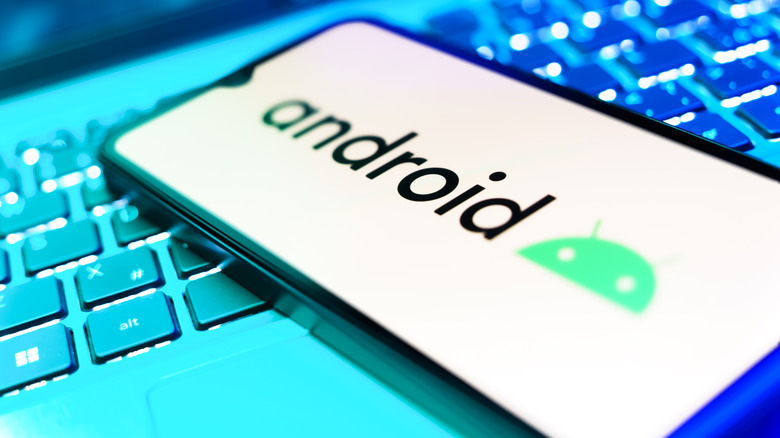 A smartphone displaying the Android logo rests on top of a keyboard illuminated by light and dark aqua colors
