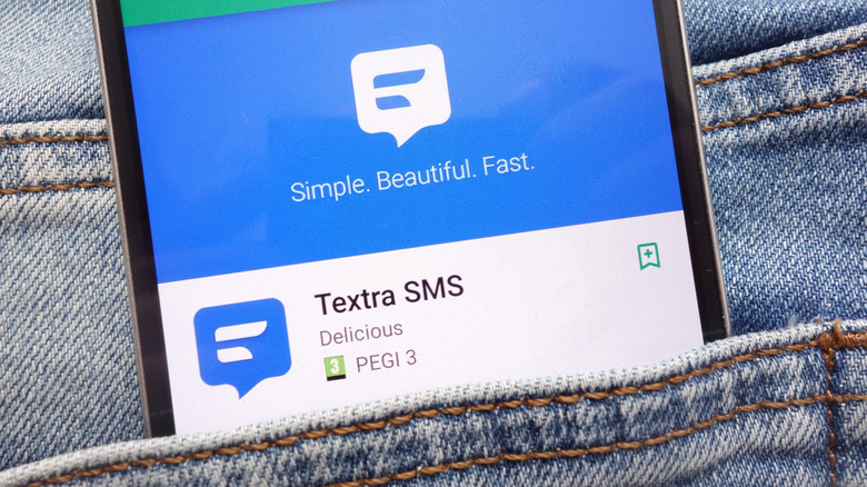 A smartphone in the back pocket of a pair of jeans, the phone is displaying Textra SMS within the Google Play Store