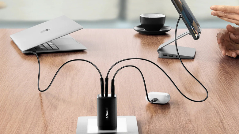 A power adapter plugged into an outlet on a table with a MacBook and iPad plugged in