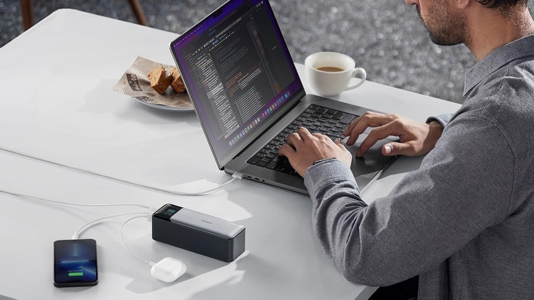 A person using a MacBook with Anker 737 Power Bank charging the laptop and other gadgets