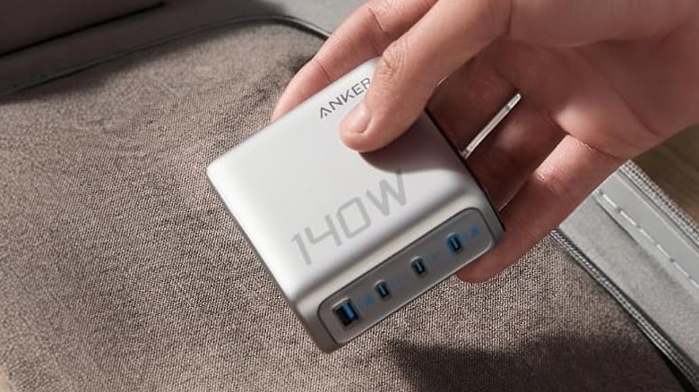 Close-up of a person holding Anker's 140W charger above a piece of luggage