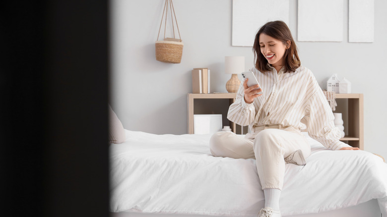 Woman using phone while on bed in minimalist bedroom