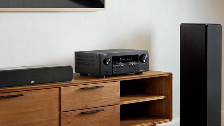 The Denon AVR-S970H AV receiver set up on an entertainment center in a modern living room, powering a set of speakers.